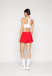 Pantaloni sportivi rossi con vestibilità rilassata, abbinati a una canotta bianca e calzini bianchi. Sono visibili un tessuto liscio e una cintura elasticizzata.