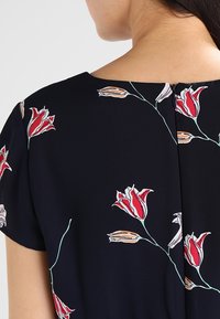 Musta mekko, jossa on punaisia, vaaleanpunaisia ja vihreitä kukkakuoseja, lyhyillä hihoilla ja takana vetoketjukiinnitys. Silkkiinen kangas.