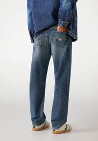 Lichtblauwe denim jeans met een losse pasvorm, voorzien van zichtbare stiksel, een patchlogo op de achterzak en een vervaagde textuur.