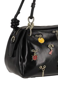 Fekete bőrből készült kézitáska, ráncolt dizájnnal, arany színű fém kiegészítőkkel és dekoratív medálokkal, köztük egy mosolygós arc és egy katicabogár.