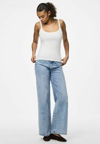 Top blanco de canalé con tirantes anchos, combinado con pantalones vaqueros de pierna ancha en azul claro. El conjunto tiene un diseño casual y estructurado.