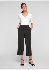 Zwarte wijde broek met een trekkoord in de taille, gedragen met een aangesloten witte V-hals top. De outfit heeft een gladde textuur en een cropped lengte.