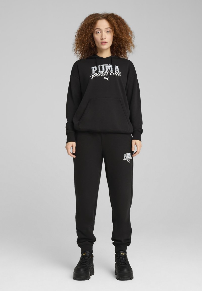 Zwarte fleece hoodie met het logo "PUMA sports club", gecombineerd met bijpassende joggingbroek. Beide hebben een relaxed fit en een voorzak.