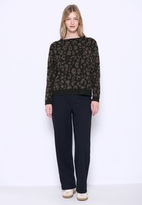 Maglione a maglia con stampa leopardata in marrone scuro, dalla vestibilità ampia, abbinato a pantaloni larghi blu scuro e sneakers di colore chiaro.