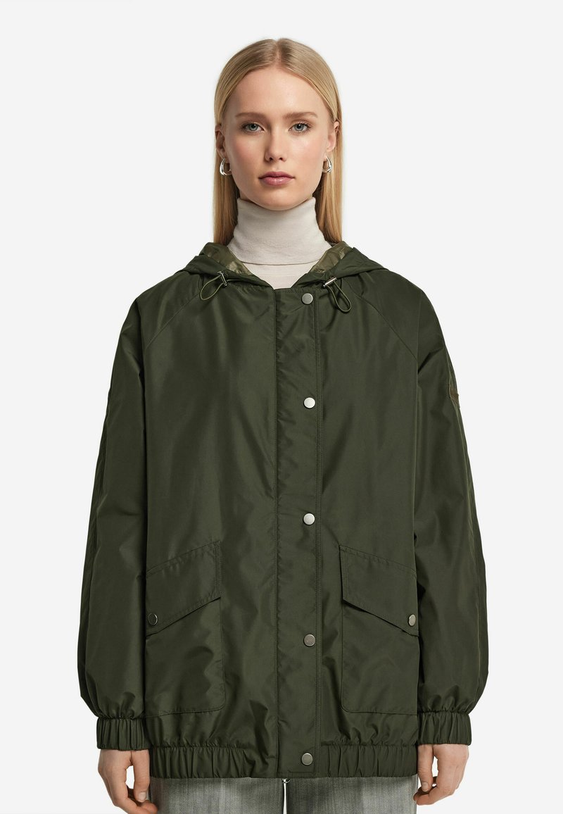 Olivenfärgad lätt jacka med huva, elastiska ärmmuddar och två framfickor. Har tryckknapps-stängning och dragsko i nederkant.