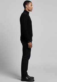 Suéter negro acanalado con cuello alto, combinado con jeans oscuros y botas de cuero negras. Vista lateral que resalta la silueta y textura.