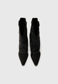Bottines en daim noir avec des pointes effilées, arborant des coutures blanches décoratives et une tige de hauteur moyenne. Texture lisse, design minimaliste.