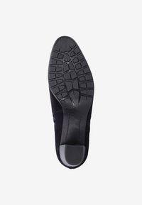 Suela de zapato de ante negro con goma texturizada para un buen agarre. Presenta una punta redondeada y un ligero tacón para mayor estabilidad. Marcas y detalles de tamaño visibles.