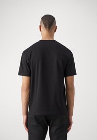 Svart kortermet t-skjorte med rund hals. Glatt bomullsstoff, avslappet passform. Sett fra baksiden, som viser et enkelt design uten dekorasjoner.