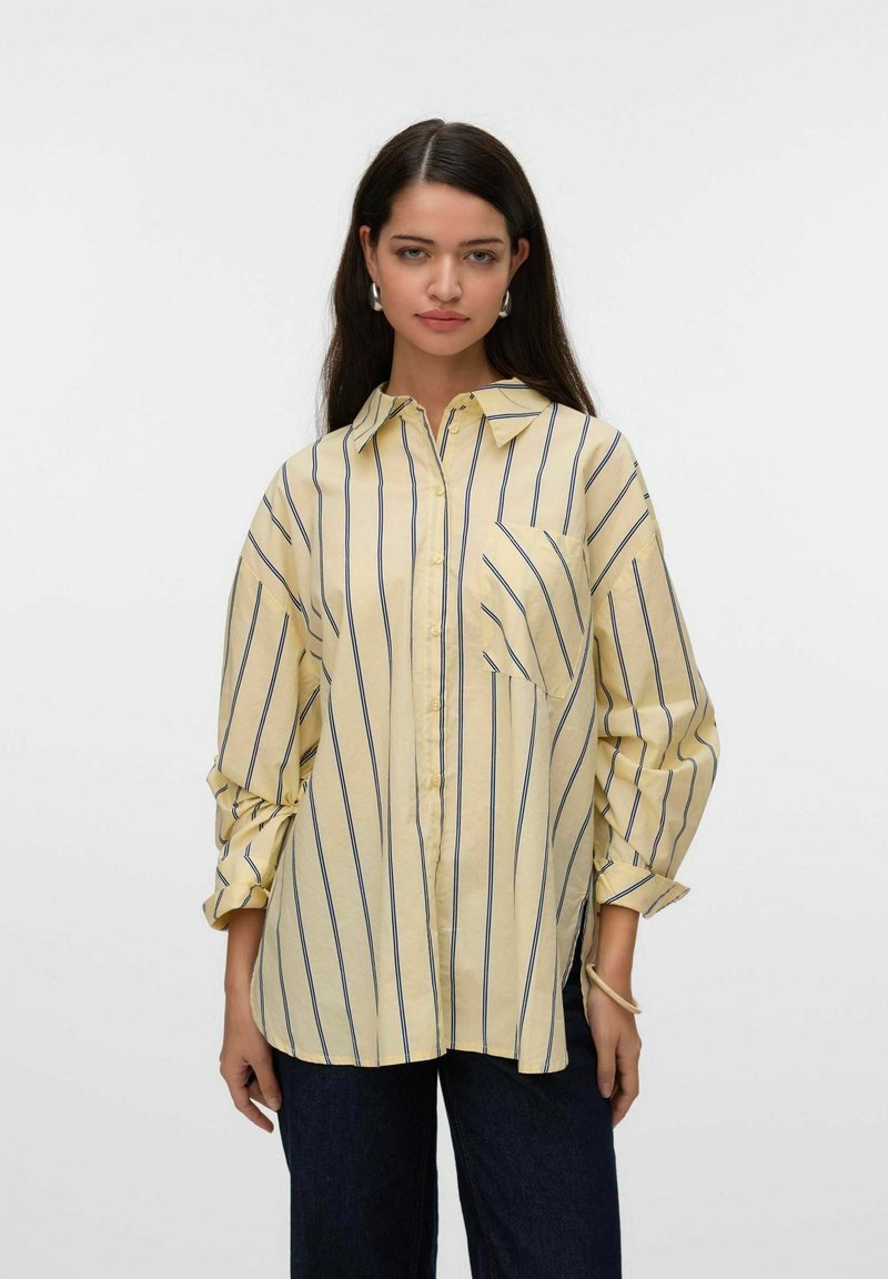 Camisa de rayas amarillas con cuello, botones en la parte delantera y bolsillo en el pecho. Tejido suave y corte relajado con mangas enrolladas.