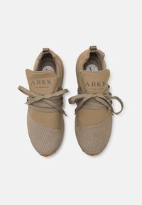 Beige sneakers met geperforeerde textuur, vetersluiting, gevoerde kraag en contrasterende oranje accenten op de zool. ARKK branding op de tong.