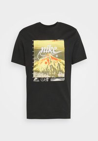 Svart bomull t-shirt med en grafik av en vulkan och "Nike"-text i vitt på en gul bakgrund, med ytterligare designelement nedan.