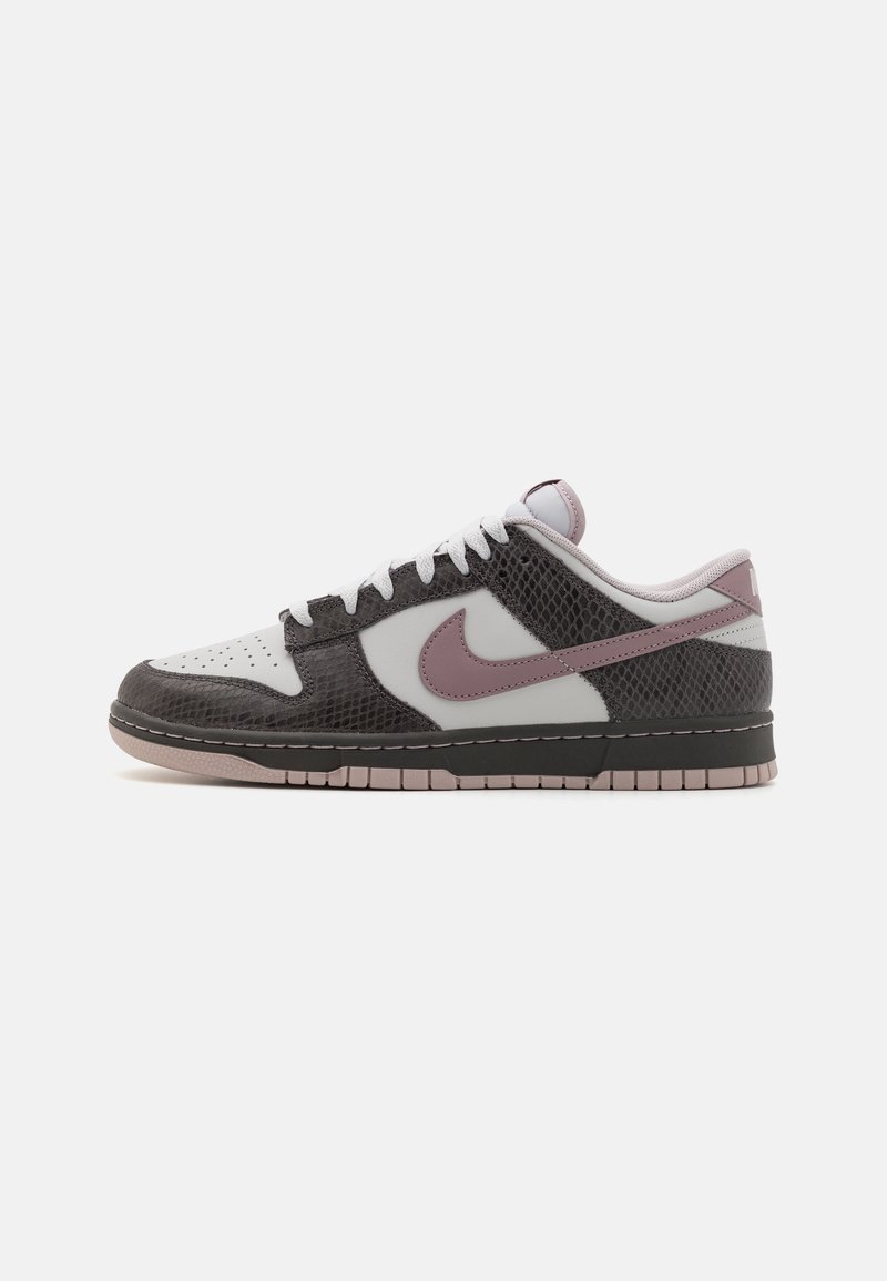 Lage sneaker met een witte basis, donkerbruine textuur-overlays, mauve Nike swoosh, witte veters en mauve zoolaccenten op een witte achtergrond.
