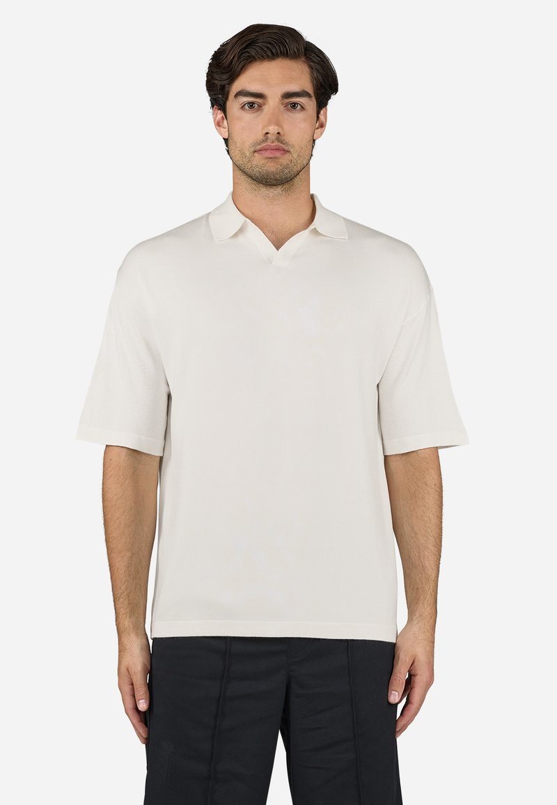 Short-sleeve, cream polo shirt made from soft fabric. Features a V-neck collar and relaxed fit, with minimal stitching detail.
