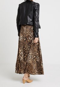 Černá kožená bunda s detaily na ramenou, nošená přes maxi sukni s leopardím potiskem v přírodních tónech a s plynulým střihem. Světle hnědé mule s podpatkem.