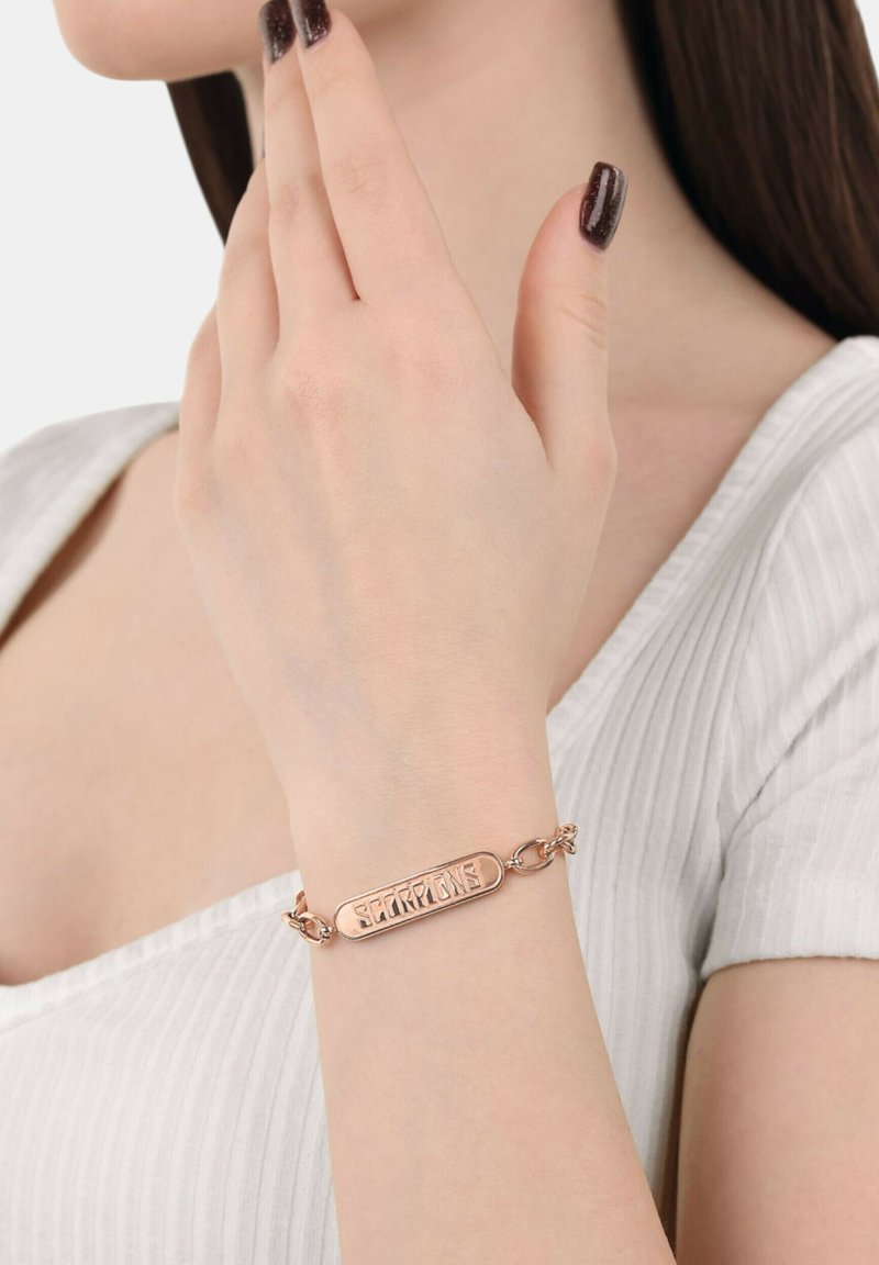 Pulsera en oro rosa con una placa rectangular grabada con la palabra "Escorpiones". Conectada por una cadena con eslabones redondos. Acabado liso.