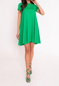 Grünes, ärmelloses A-Linien-Kleid aus weichem Stoff, mit rundem Ausschnitt und fließendem Design, kombiniert mit grünen Riemchenabsätzen.