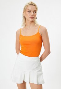 Orangeanpassad tanktop med tunna axelband, tillsammans med en vit volangkjol i mini modell. Slätt material och enkel design, lämplig för avslappnad klädsel.