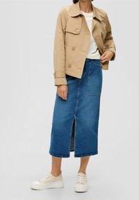 Béžový trenčkot s dvojitým zapínáním na knoflíky, modrá džínová maxi sukně s předním rozparkem a bílé tenisky na platformě.