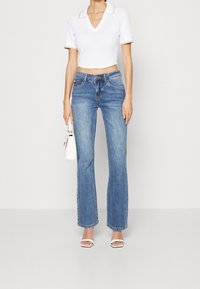 Chemise polo blanche courte avec texture côtelée, associée à un jean évasé bleu clair. Accentuée d'un petit sac à main blanc et de talons blancs à lanières.