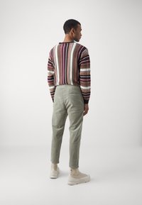 Sweater in dark red and cream stripes, paired with light green corduroy pants. Casual sneakers in beige complete the outfit.