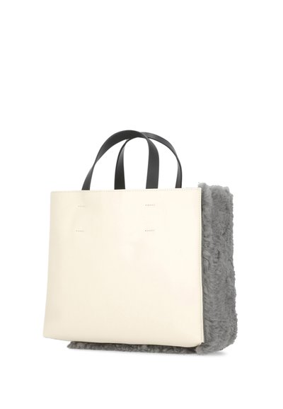 Borsa tote con un corpo liscio color crema, manici neri e un pannello laterale in pelliccia grigia testurizzata. Presenta una cucitura minimalista sul davanti.
