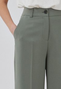 Olive green tailored pants with a smooth texture, a single button closure, side pockets, and a straight-leg design.
