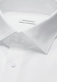 Chemise blanche à col pointu, deux boutons visibles et une étiquette à l'intérieur du col indiquant "seidensticker."