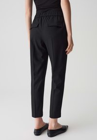 Pantaloni neri su misura con un alto girovita elasticizzato, due tasche posteriori e una vestibilità slim che si restringe alla caviglia, realizzati in tessuto liscio.