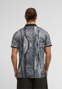 Fekete és szürke mintázatú pólóing, galléros nyakkal és rövid ujjakkal; jellegzetessége a textúrált grafikai dizájn és a kontrasztos kiegészítők.