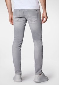 Jasnoszare, dopasowane dżinsy o gładkiej fakturze, z dwoma tylnymi kieszeniami. W połączeniu z białymi trampkami, widok z tyłu.