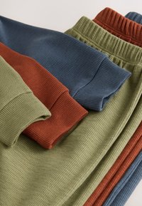 Ropa de descanso de algodón con punto acanalado en verde oliva, rojo óxido y azul marino. Presenta puños y cinturillas elásticas, mostrando patrones texturizados.