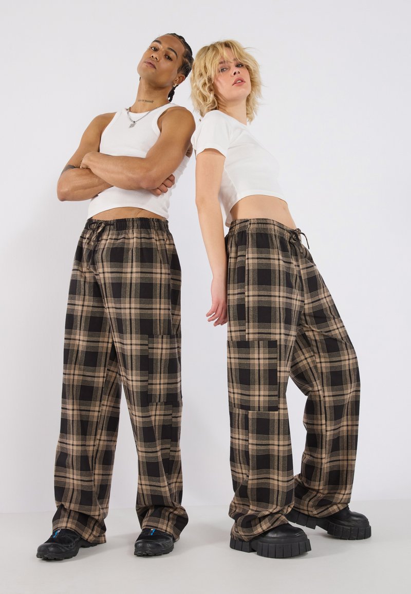 Bruine en zwarte geruite wijde broek, met een elastische tailleband en zijzakken, gecombineerd met witte crop tops en stevige zwarte schoenen.