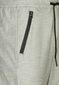 Hellgraue Sporthose aus strukturiertem Stoff, mit einer schwarzen Reißverschlusstasche und einem verstellbaren Kordelzug an der Taille.
