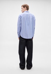 Gestreiftes blau-weißes Hemd mit Knöpfen, langen Ärmeln und abgerundetem Saum, getragen mit dunkelblauen Denim-Jeans mit Gesäßtaschen. Schlichtes Design, legere Passform.