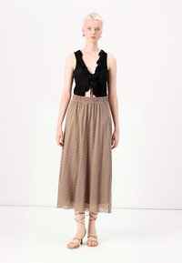 Un haut noir à volants et liens à l'avant, associé à une jupe beige, longueur genou, ornée d'un motif à pois et d'une taille élastique.