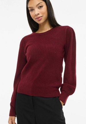 Burgundi värvi kootud kampsun tekstuurse pinnaga, ümmarguse kaelusega ja pikkade varrukatega. Omab keha järgivaid varrukakotte ja sirget ääreosa.