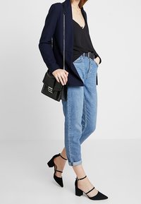 Svart kavaj, svart tanktopp, ljusblå högmidjade jeans, svarta klackskor med ankelsnören och en svart handväska med nitar.