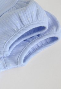 Morbidi muffole azzurro chiaro per neonati con pois bianchi e polsini elasticizzati a coste su uno sfondo bianco semplice.