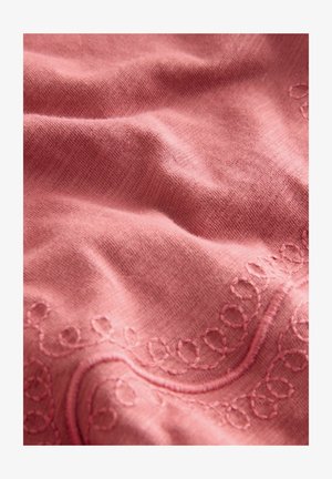 Tessuto rosa con ricami che presentano motivi a spirale lungo il bordo. Tessuto morbido e testurizzato con un aspetto liscio e delicato.