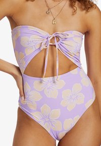 Maillot de bain une pièce sans bretelles de couleur violet avec un imprimé floral en beige clair, présentant un design découpé et un lien réglable à l'avant.