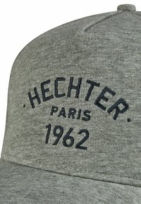 Grijze pet van textuurstof met geborduurde tekst "HECHTER PARIS 1962" in donkerblauw, met een ronde kroon en een stijve klep.