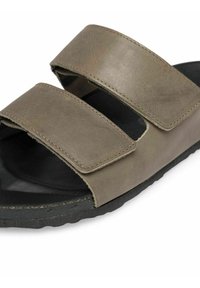 Sandale en cuir marron avec deux larges sangles réglables, légère texture et semelle en caoutchouc noire. Présente un design minimaliste et des détails de couture.