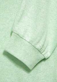 Světlý zelený svetr s jemnou texturou. Rukáv má žebrované detaily, které zdůrazňují ležérní design.