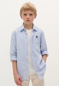 Lichtblauw gestreepte button-up shirt van een zachte stof, met een kleine zwarte schedel geborduurd op de borst, met opgerolde mouwen en een ontspannen pasvorm.