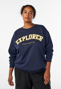 Jūrininkų bliuzonas su dideliu geltonu užrašu „EXPLORER“ kreivai išdėstytu. Minkšta medžiaga, su guma apdirbtais rankogaliais ir laisvu siluetu.