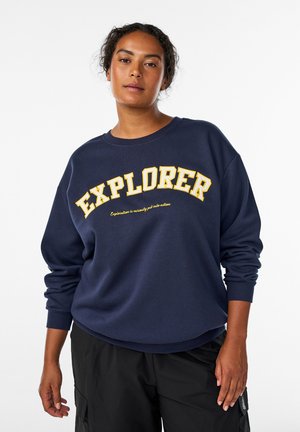 Námornícky sveter s veľkým žltým textom "EXPLORER" v zakrivenom dizajne. Mäkká tkanina s rebrovanými manžetami a voľným strihom.