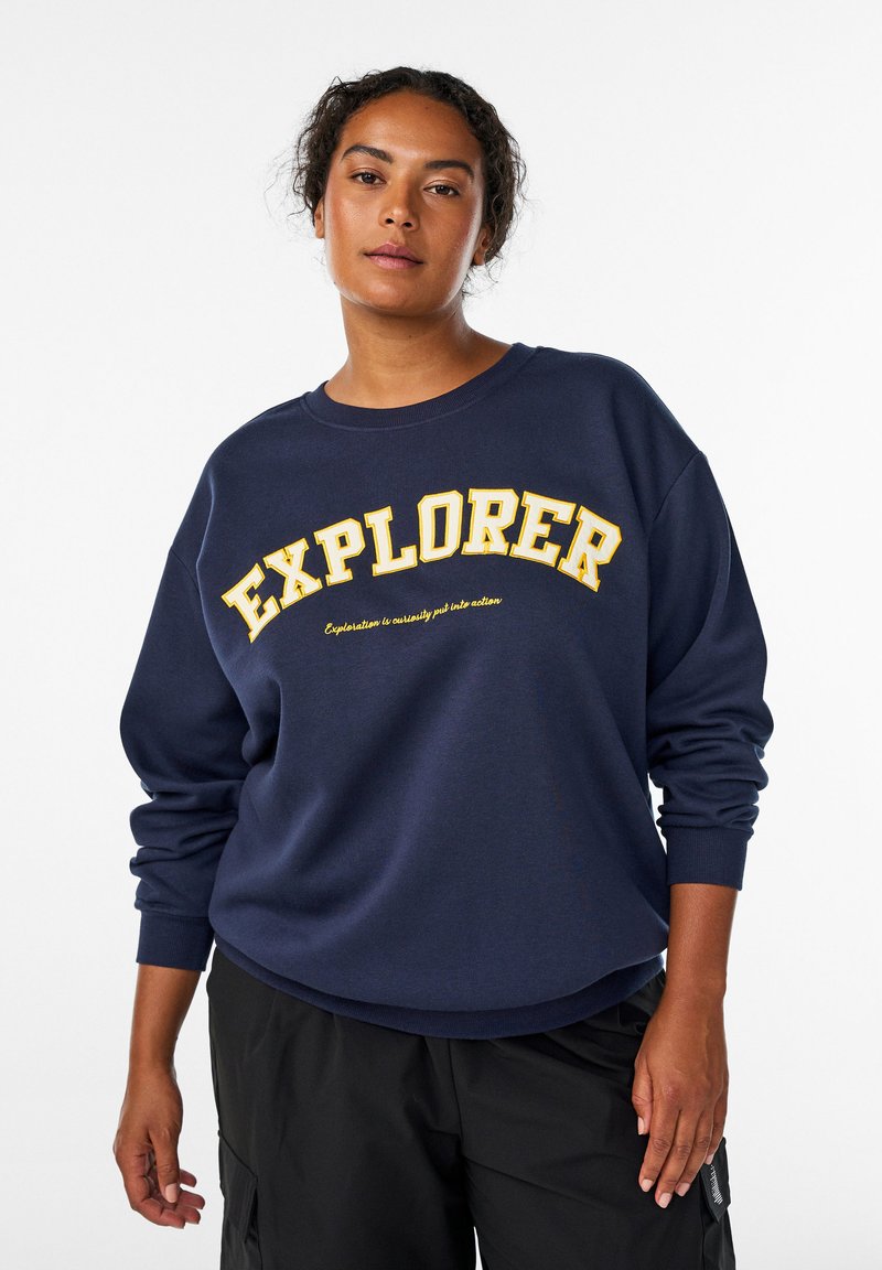 Jūrininkų bliuzonas su dideliu geltonu užrašu „EXPLORER“ kreivai išdėstytu. Minkšta medžiaga, su guma apdirbtais rankogaliais ir laisvu siluetu.