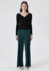 Top nero a maniche lunghe con texture a coste, abbinato a pantaloni verdi a vita alta e a gamba larga, e décolleté beige con punta.