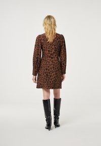 Braunes Kleid mit schwarzem Tiermuster, langen Puffärmel und tailliertem Schnitt. Kombiniert mit kniehohen, glänzenden schwarzen Stiefeln.